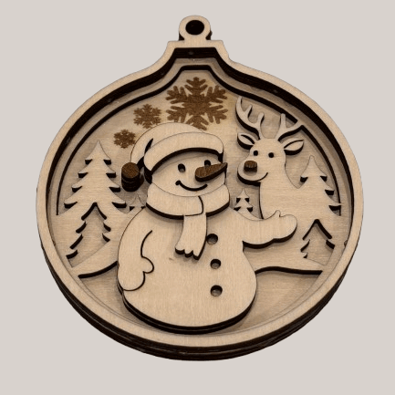 Boule de Noël en bois représentant un bonhomme de neige et un renne dans une forêt enneigée.